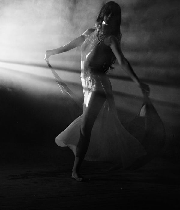 Woman performing a fluid cardio movement in a dark studio with cyan light.